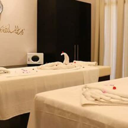 A room with two massage tables covered with white towels, a clock on the wall, and a window with curtains.