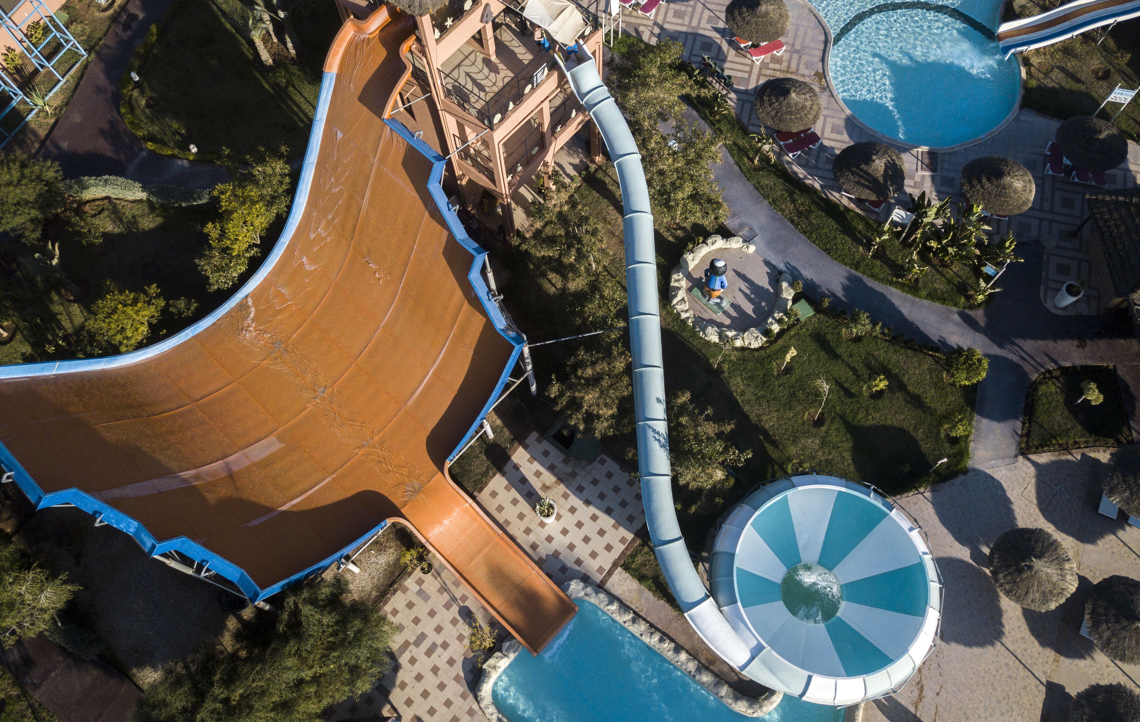 An aerial view of a water park with a large brown slide, a blue spiral slide, and a pool area.