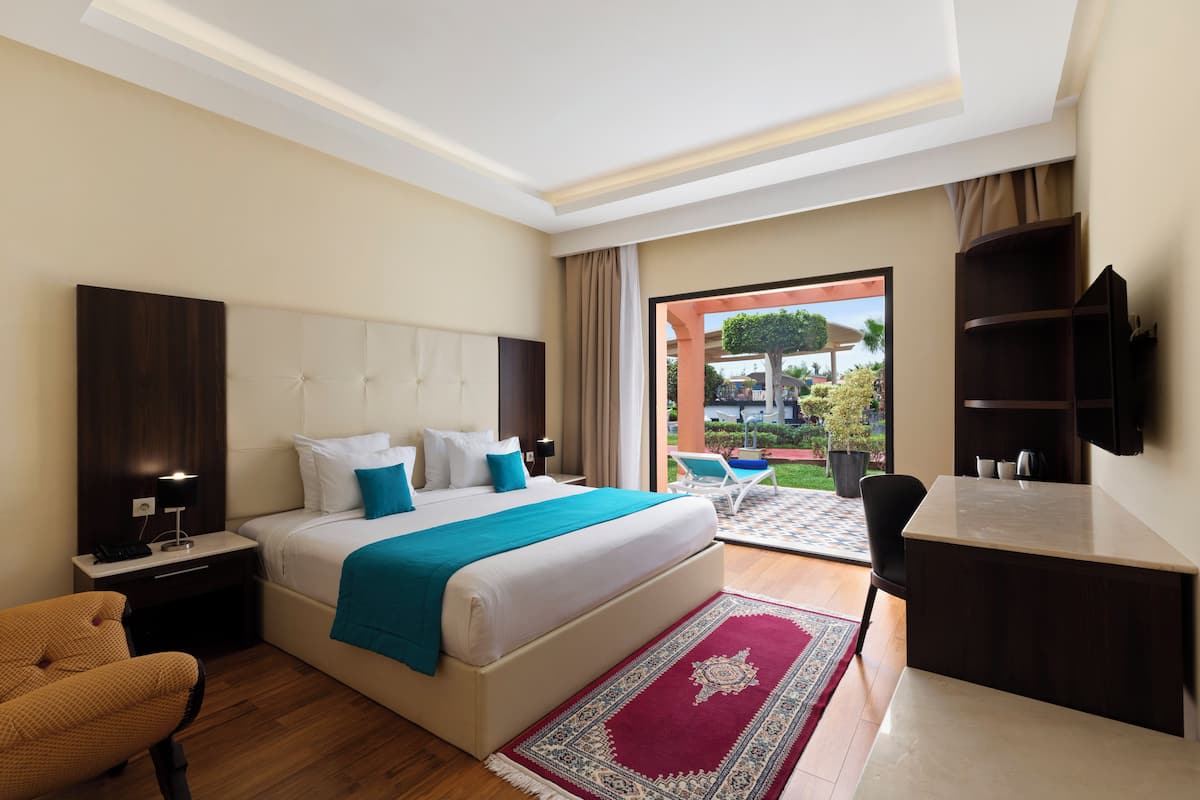 A hotel room with a bed, a desk, a chair, a nightstand, and a TV.