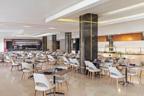 A spacious dining area with multiple tables and chairs, a central bar, and a modern ceiling design.