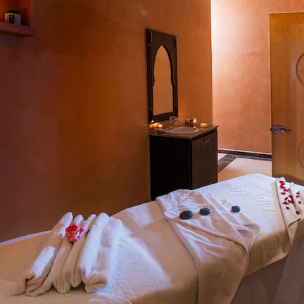 A spa room with a massage table, towels, a sink, and a mirror.