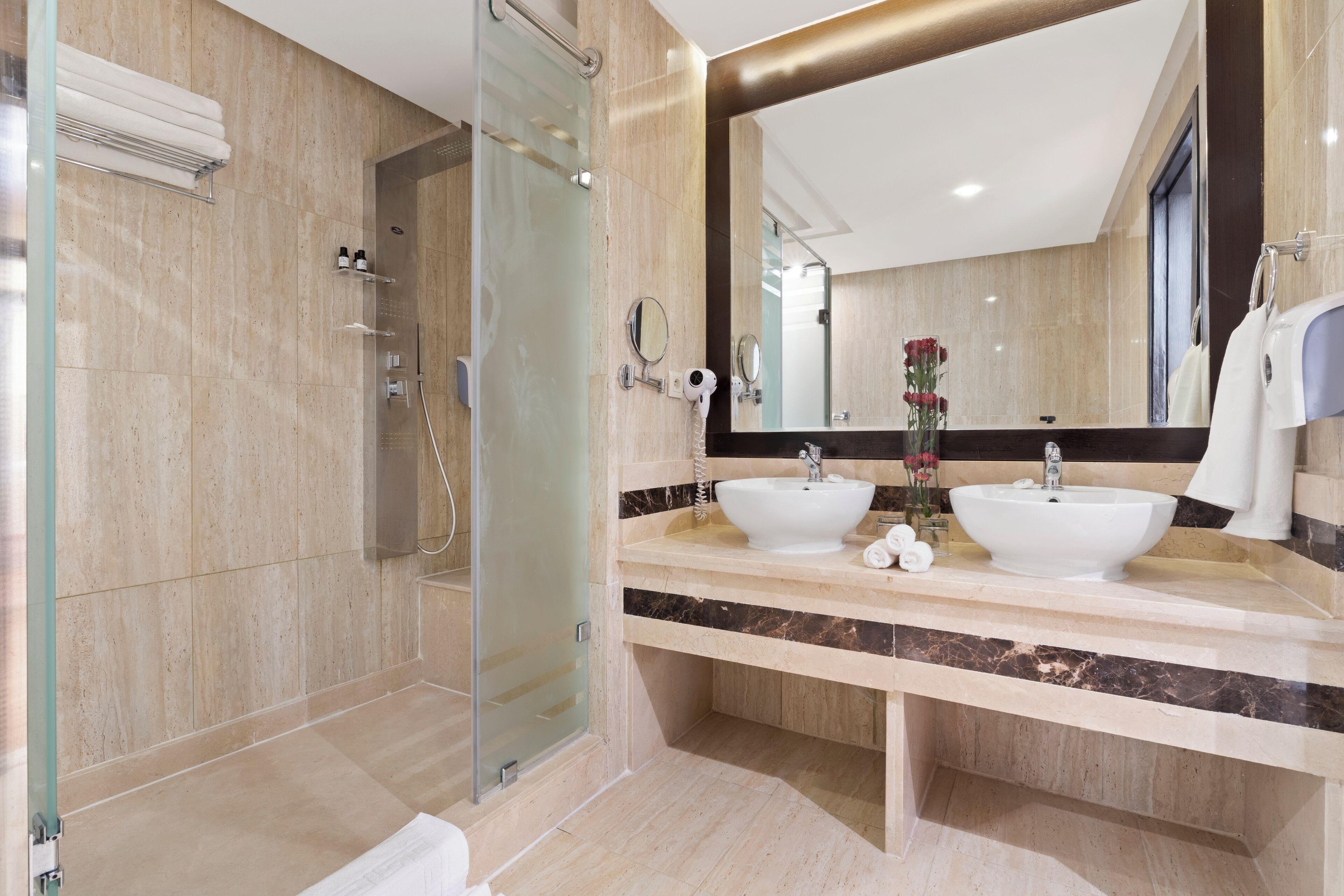 Un baño moderno con cabina de ducha de vidrio, dos lavamanos y un espejo grande.