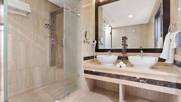 Un baño moderno con cabina de ducha de vidrio, dos lavamanos y un espejo grande.