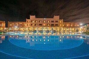 A hotel with a large pool, multiple floors, and a well-lit facade.