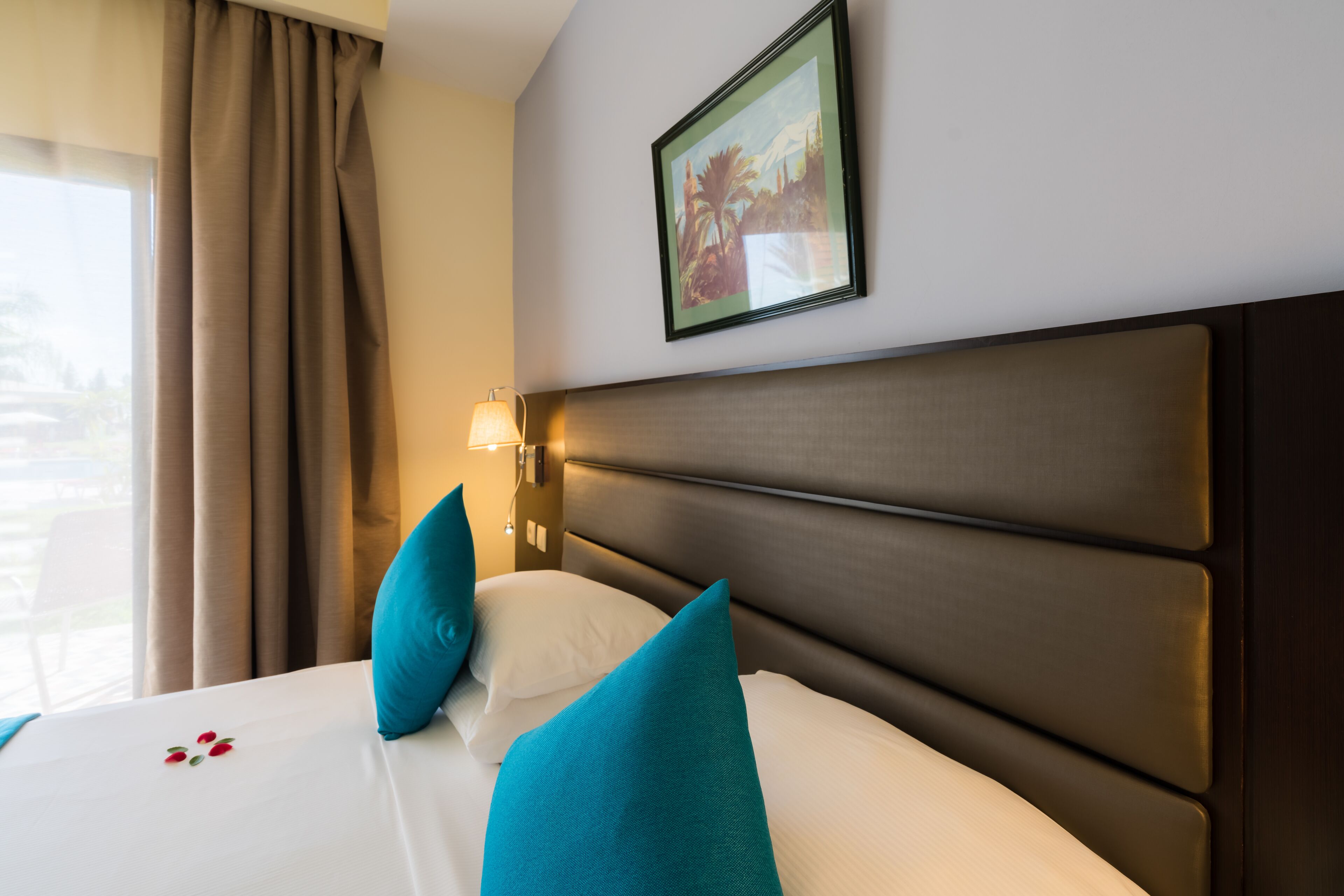 Habitación de hotel con una cama grande, dos almohadas, una mesita de noche con lámpara y un cuadro en la pared.