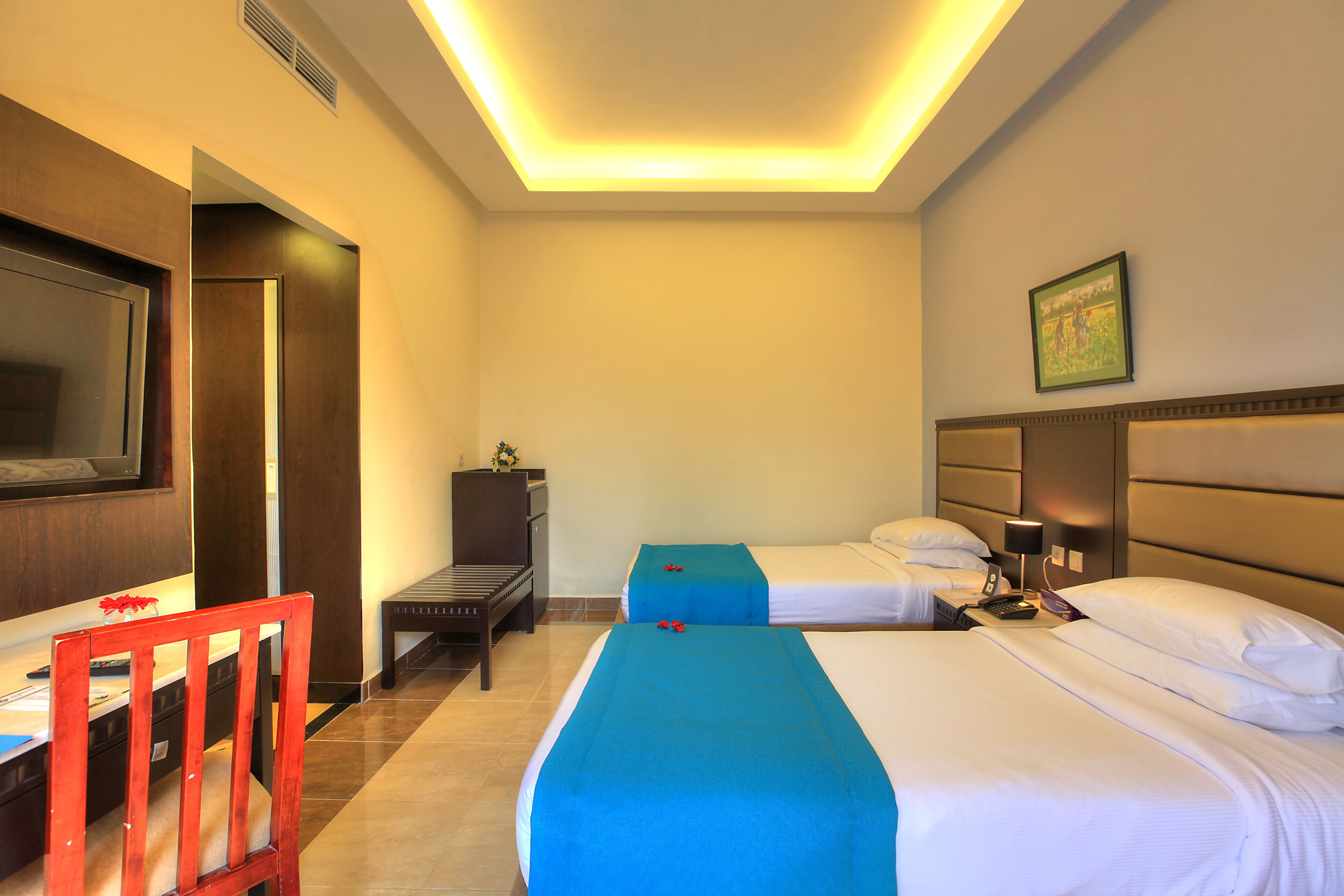 A hotel room with two beds, a desk, a TV, and a chair.