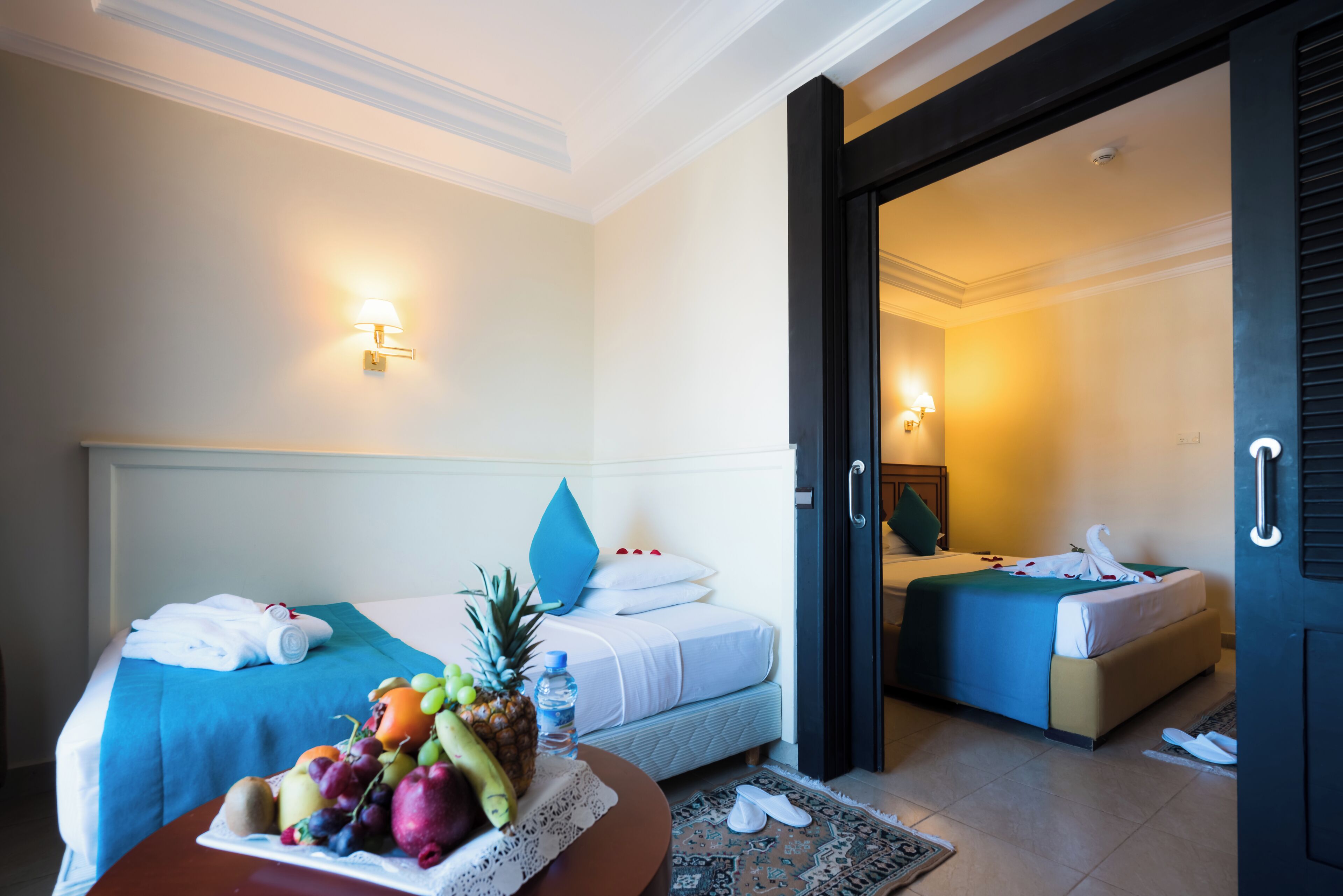 Ein Hotelzimmer mit zwei Betten, einer Obstschale auf dem Nachttisch und einer Tür zu einem anderen Raum.