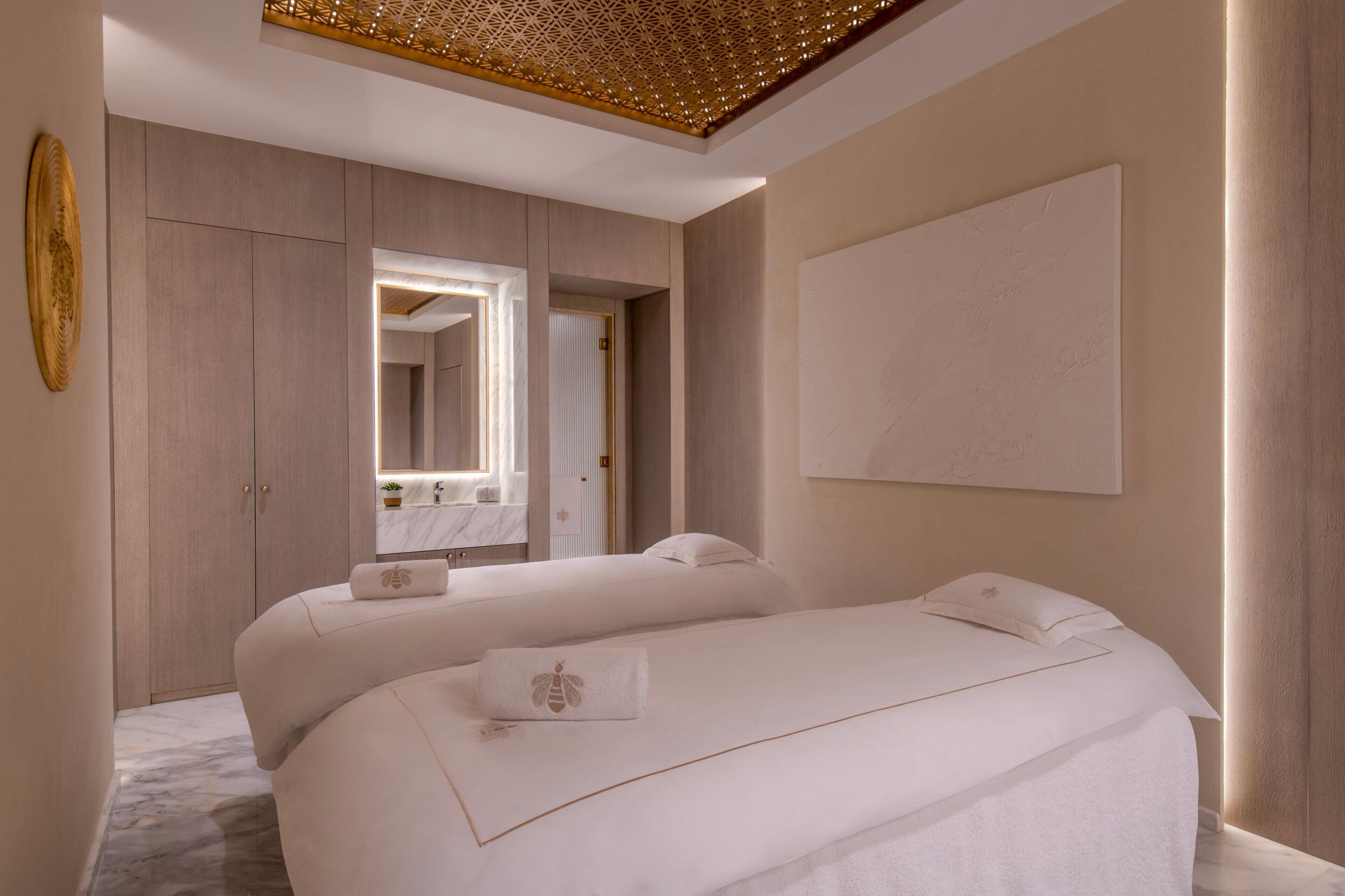 A modern hotel room with two beds, a large mirror, and a decorative ceiling.