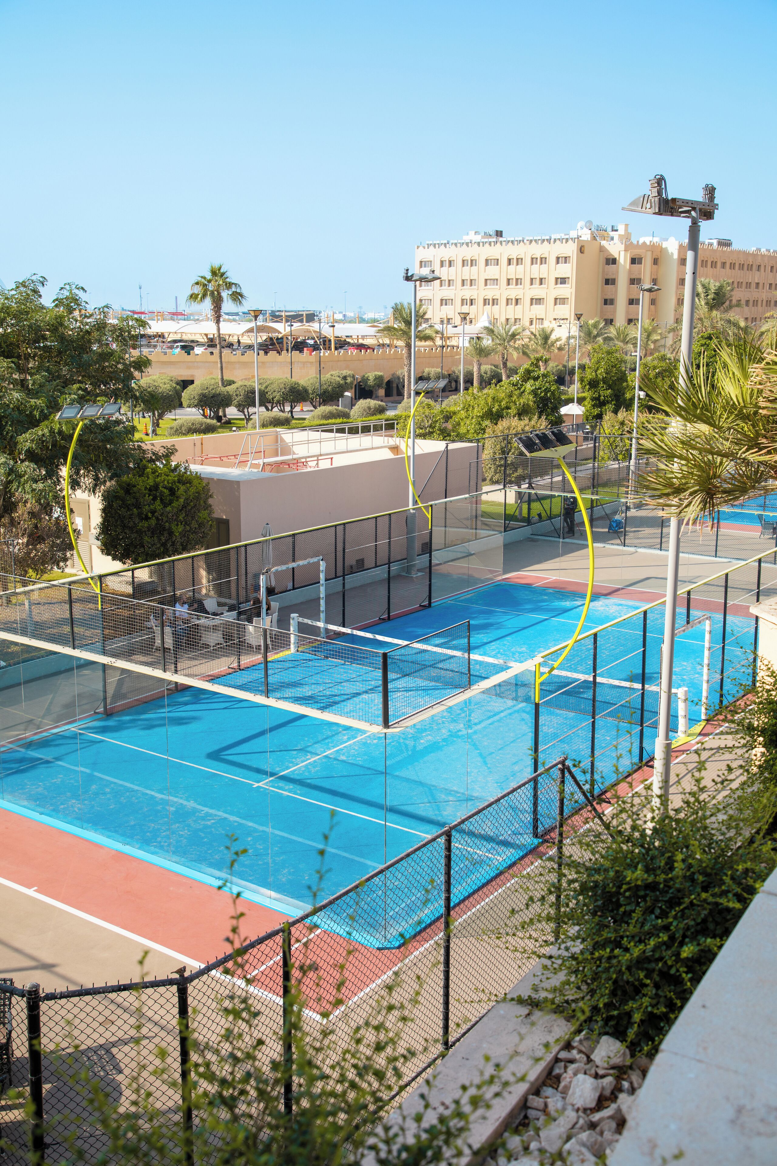 A sports court with a blue playing surface, surrounded by a fence, with a building in the background.