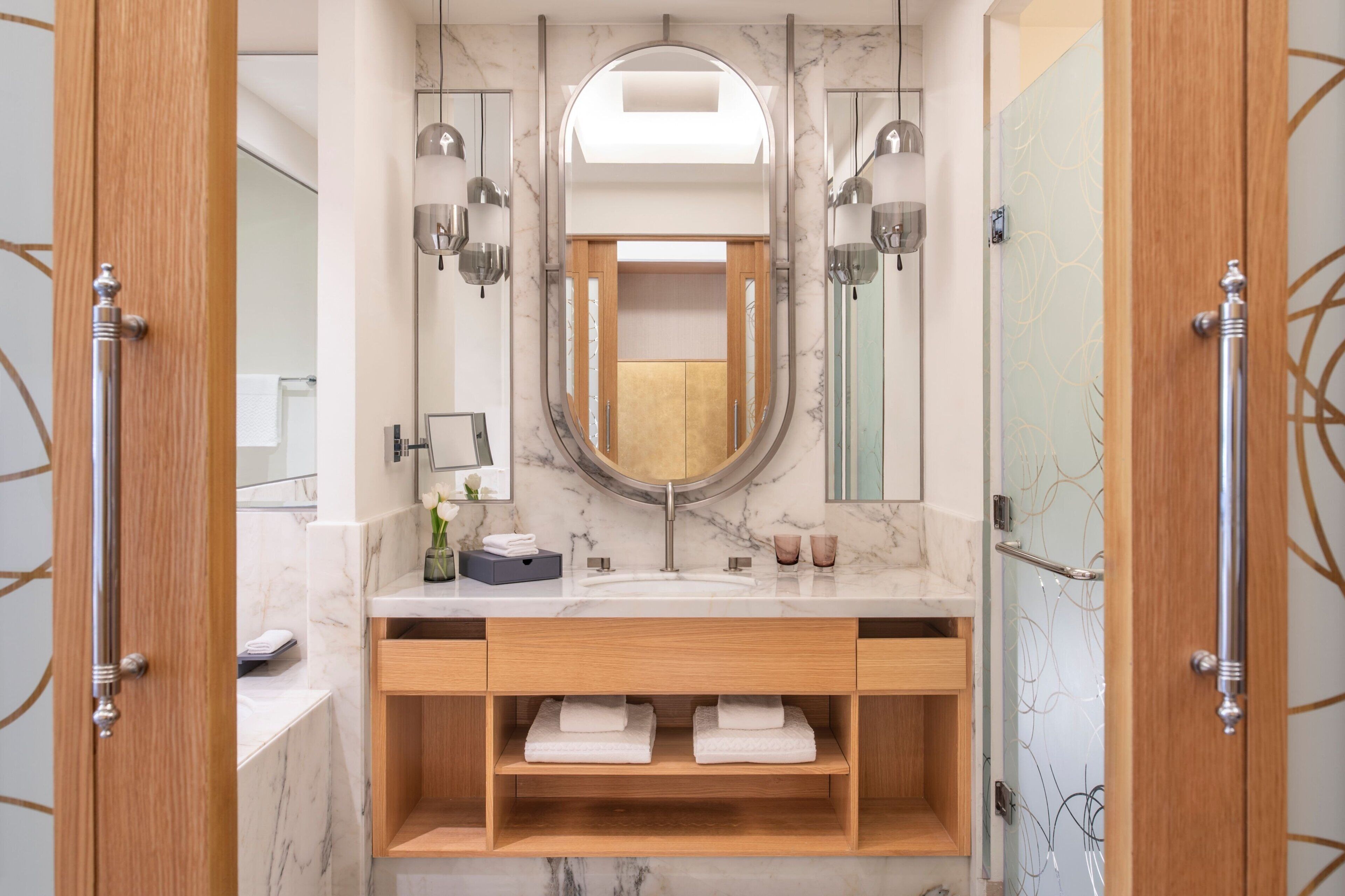 Un bagno moderno con un mobile vanità in marmo, uno specchio grande e scaffali in legno.