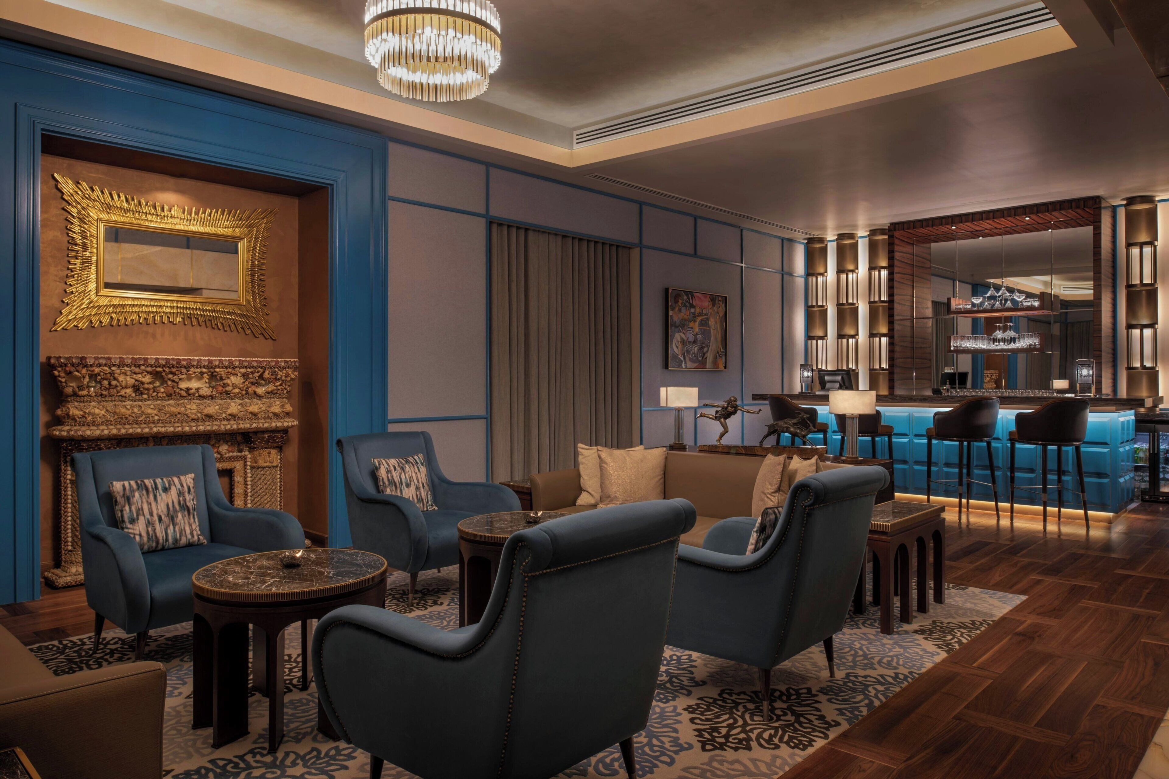 Un moderno vestíbulo de hotel con asientos tapizados en azul, una zona de bar y una chimenea decorativa.