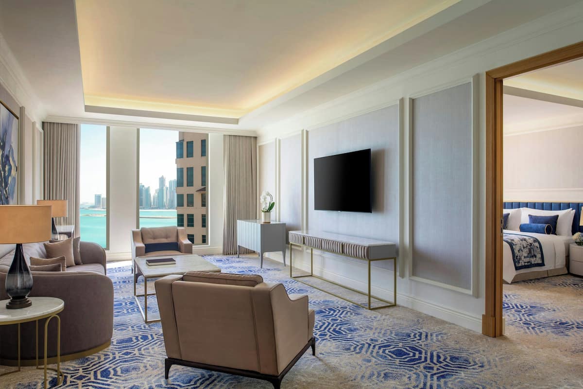 Een hotelkamer met een groot raam, een flatscreen-tv, een bank, een bijzettafeltje en een bed met een blauw hoofdeinde.