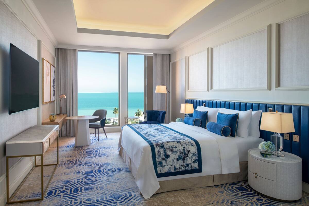 Een hotelkamer met een groot bed, een bureau, een stoel en uitzicht op de oceaan.