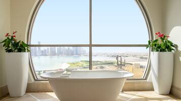 A large freestanding bathtub in a bathroom with a view of a cityscape through a large arched window.