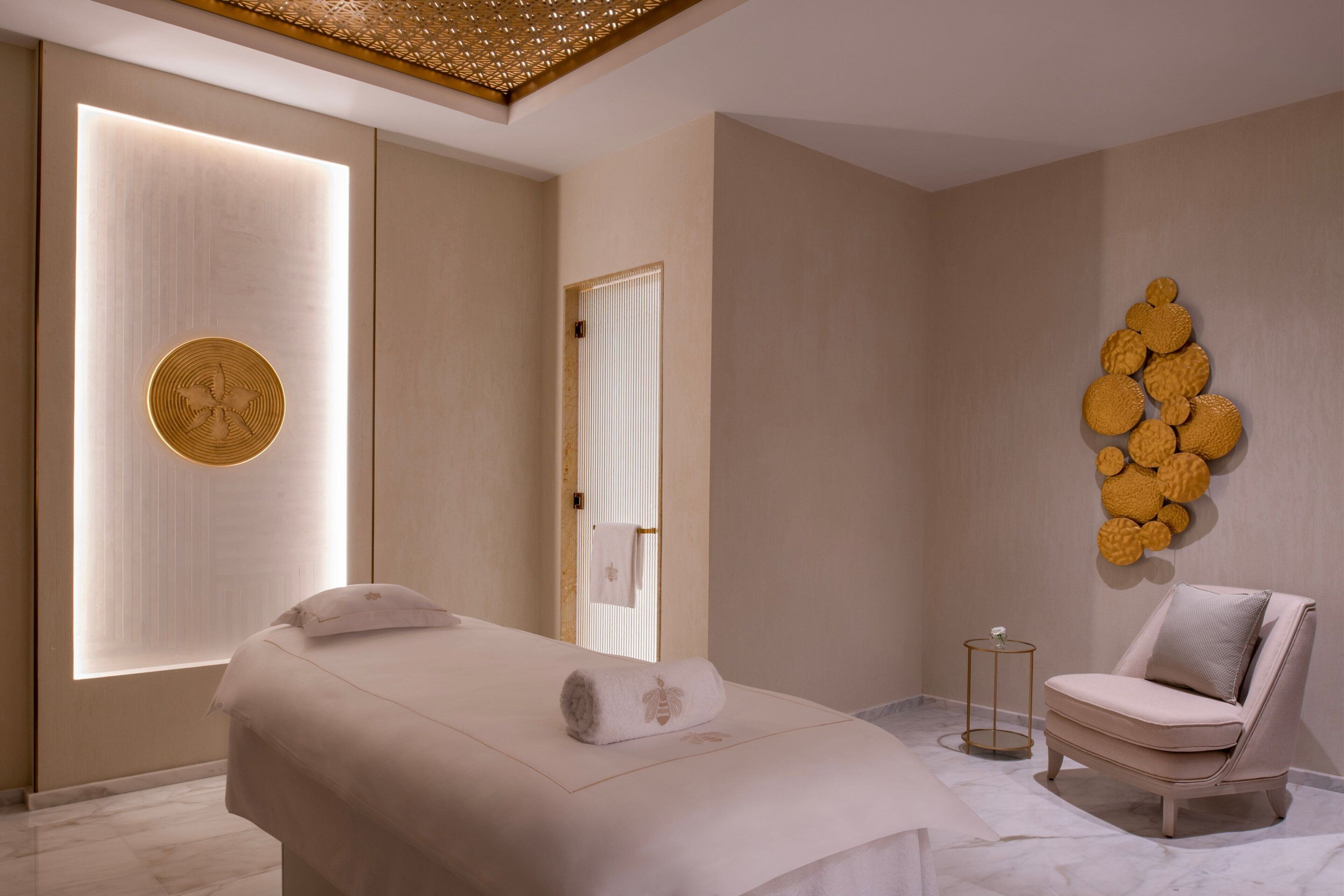 A modern spa room with a massage table, a chair, and a wall with a circular design.
