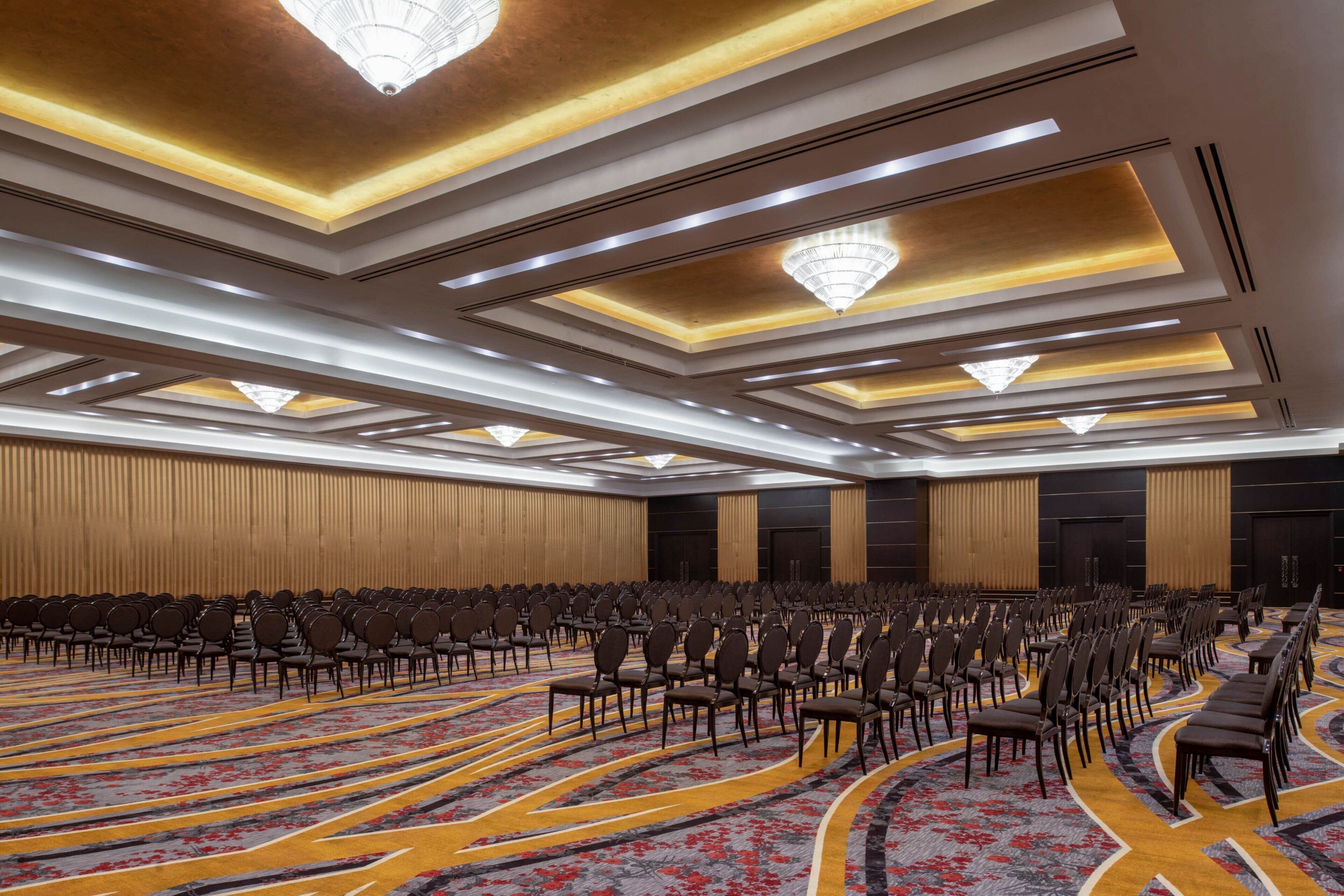 Een ruime congreszaal met rijen stoelen, een kamerbreed tapijt en een modern plafond.