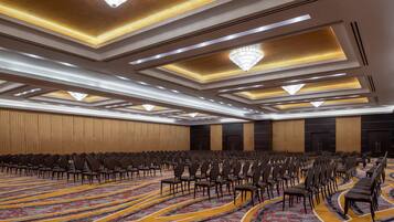 Une grande salle de conférence avec des rangées de chaises, une moquette à motifs et un design de plafond moderne.
