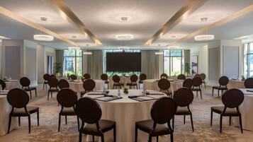 A conference room with round tables, chairs, and a large screen at the front.