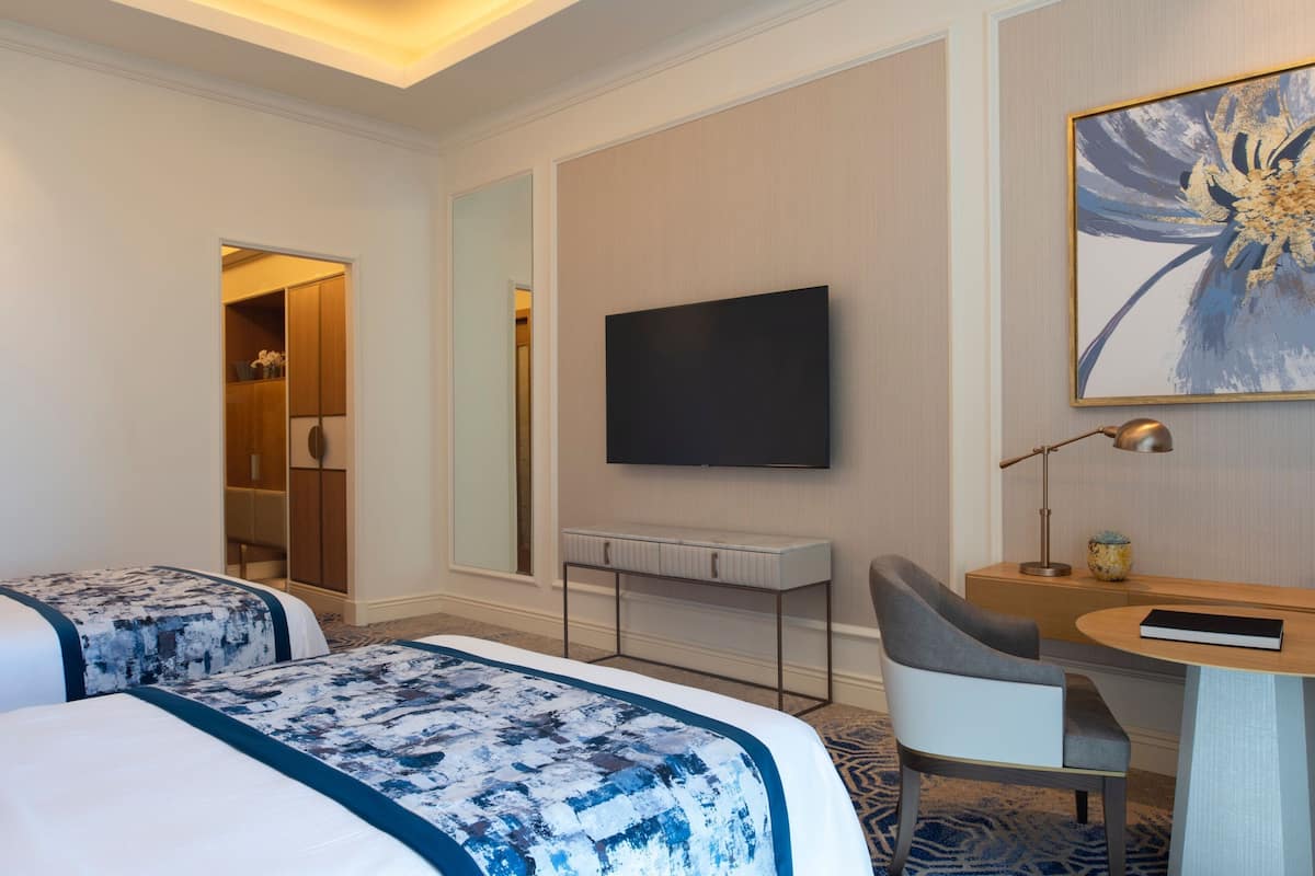 Een hotelkamer met twee bedden, een bureau, een stoel, een televisie en een grote spiegel.