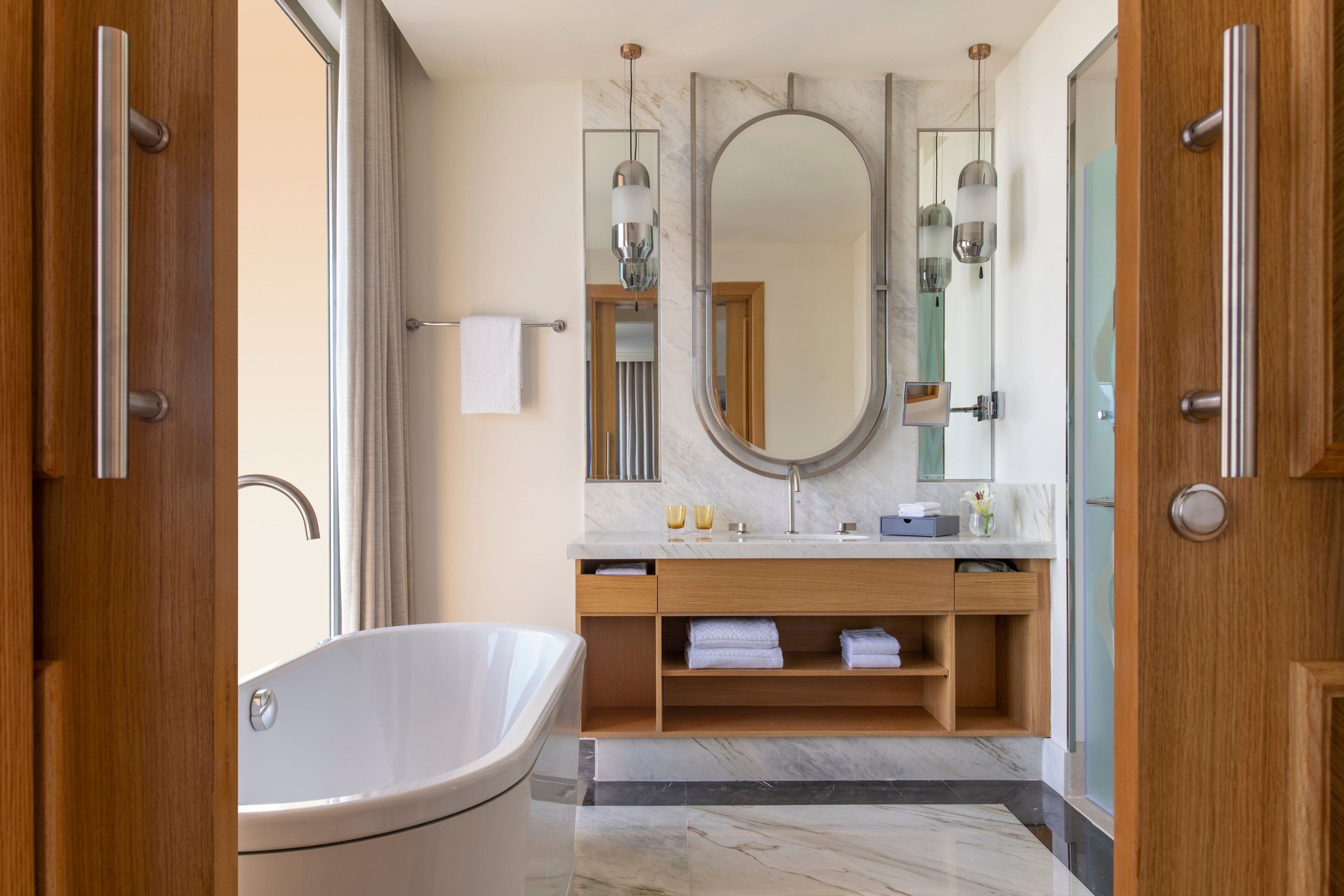 Un baño moderno con una bañera independiente, un tocador de madera y un espejo grande.
