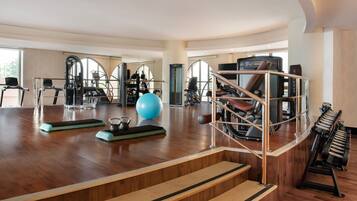 Een ruime fitnessruimte met diverse fitnessapparaten, waaronder een blauwe trainingsbal, loopbanden en een stair climber.