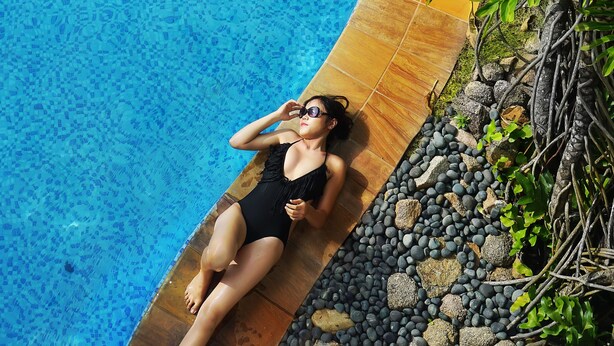 Una persona recostada en el borde de una piscina con agua cristalina y azul.