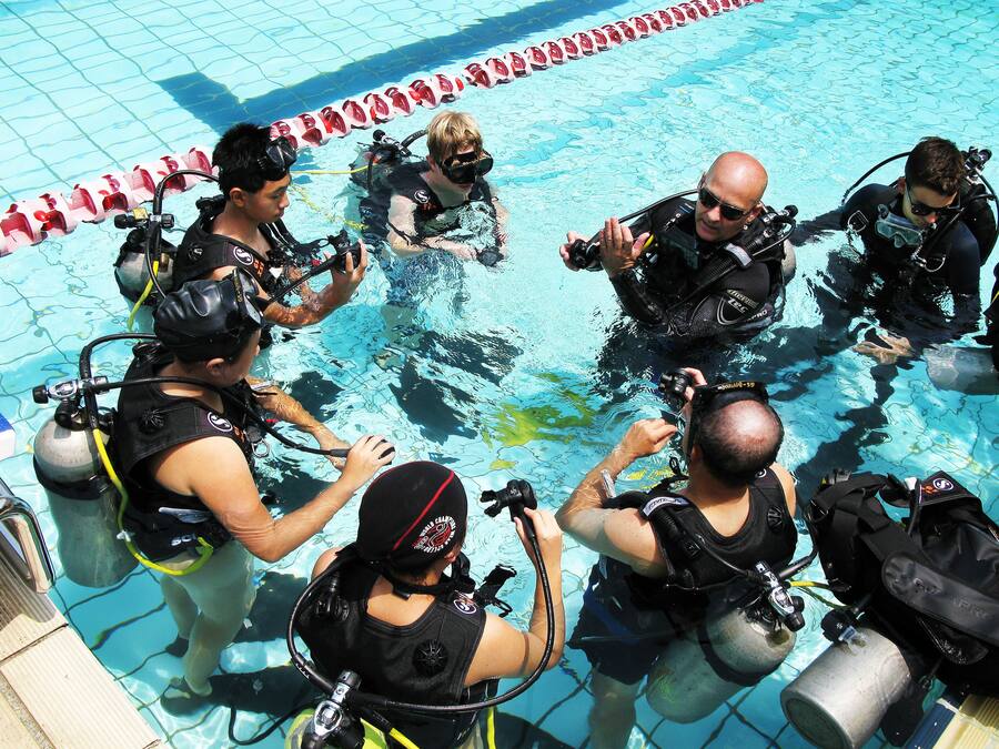 A group of scuba divers in a pool, equipped with diving gear and oxygen tanks.