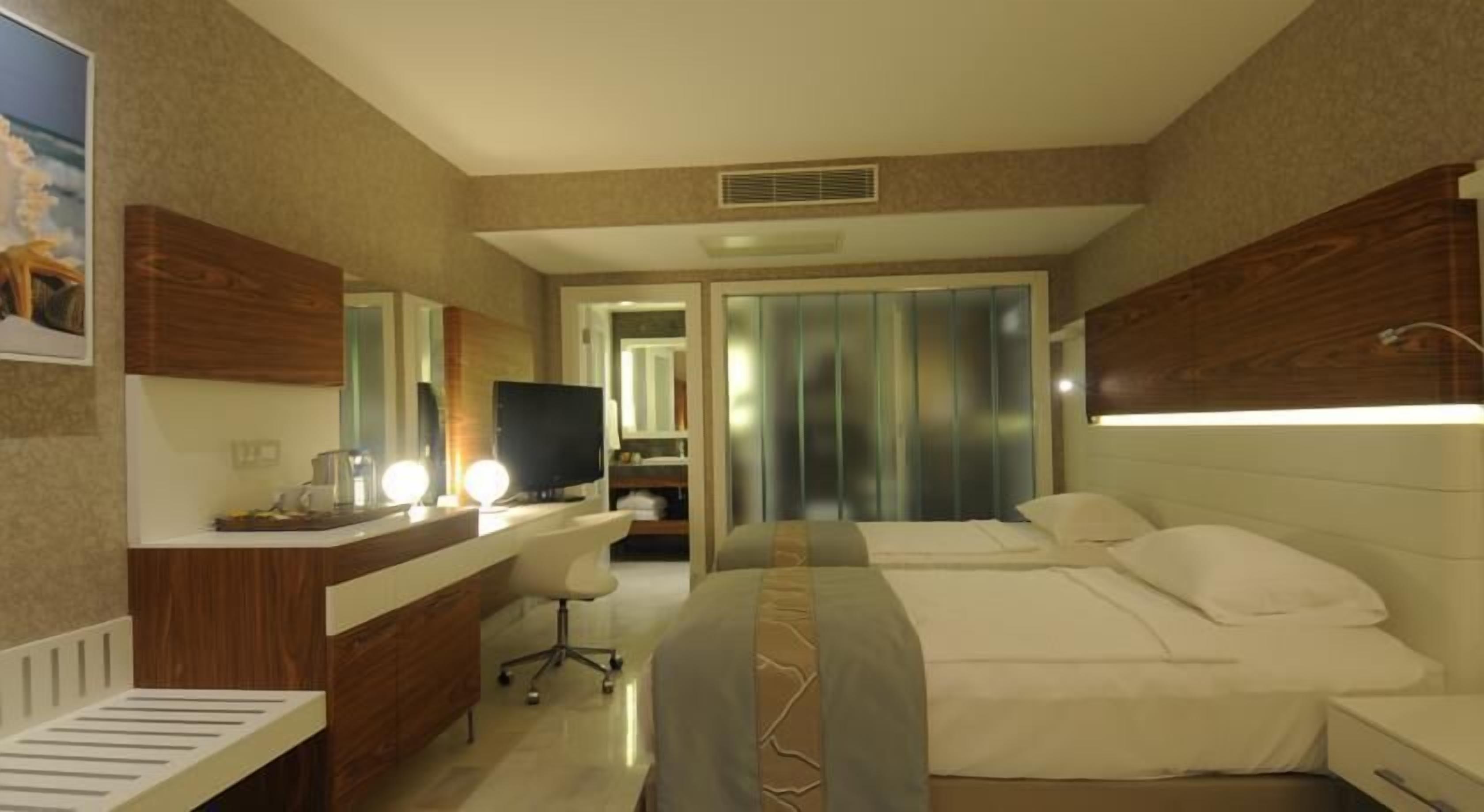 Ein Hotelzimmer mit Bett, Schreibtisch mit Computer, Stuhl und Spiegel.