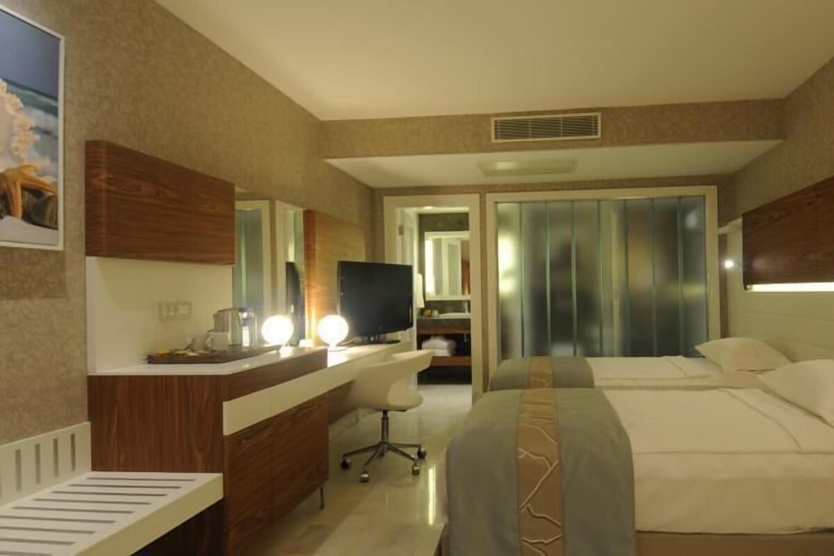 A hotel room with a bed, a desk with a computer, a chair, and a mirror.
