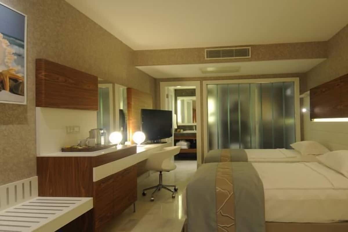 Hotellihuone, jossa on sänky, työpöytä, tietokone, tuoli ja peili.