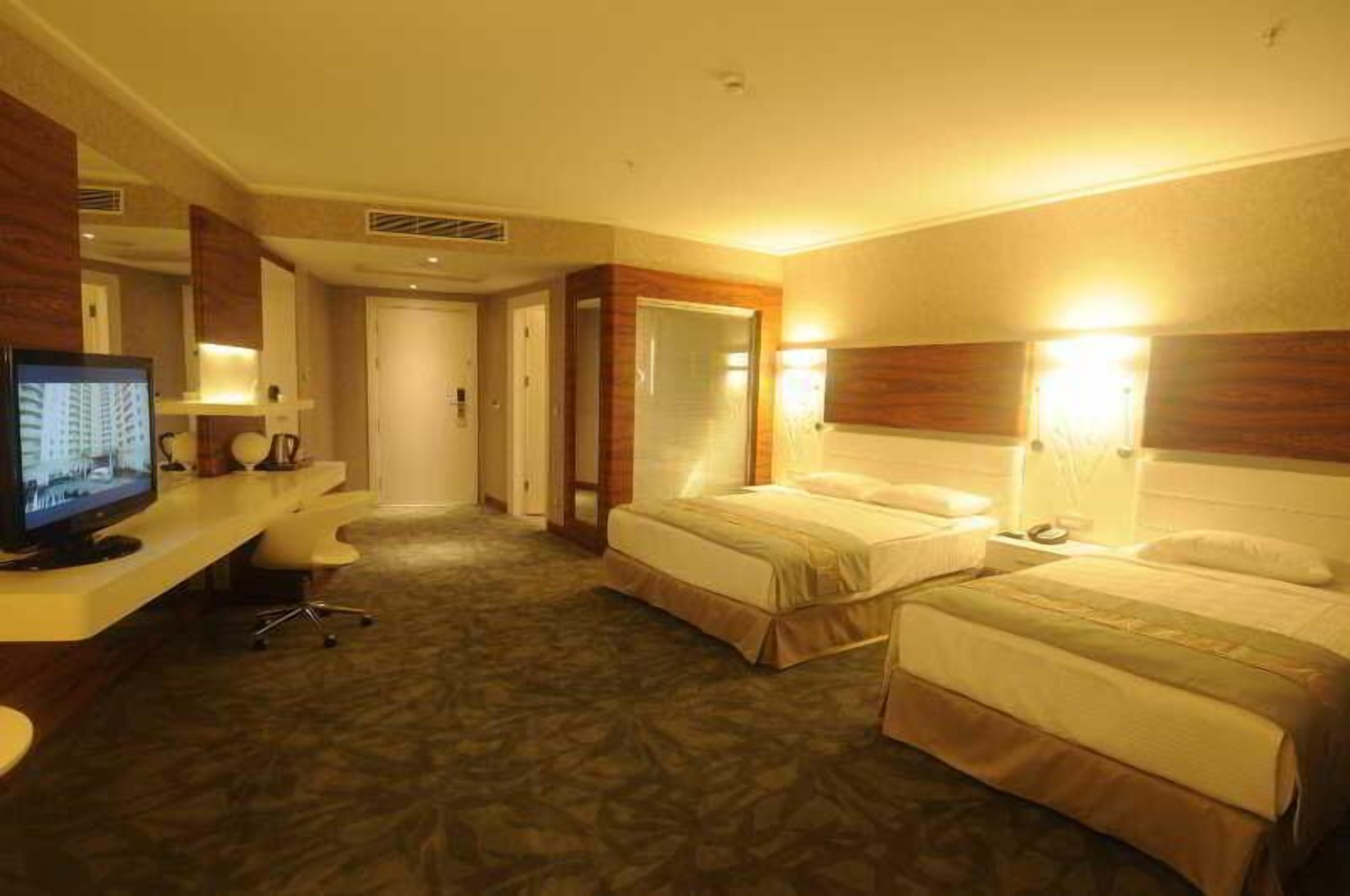 Ein Hotelzimmer mit zwei Betten, einem Schreibtisch mit Computer und einem Fernseher.