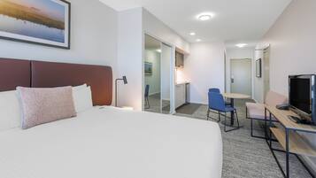 Une chambre d’hôtel avec un grand lit, un bureau avec un ordinateur, une télévision et un tableau au mur.