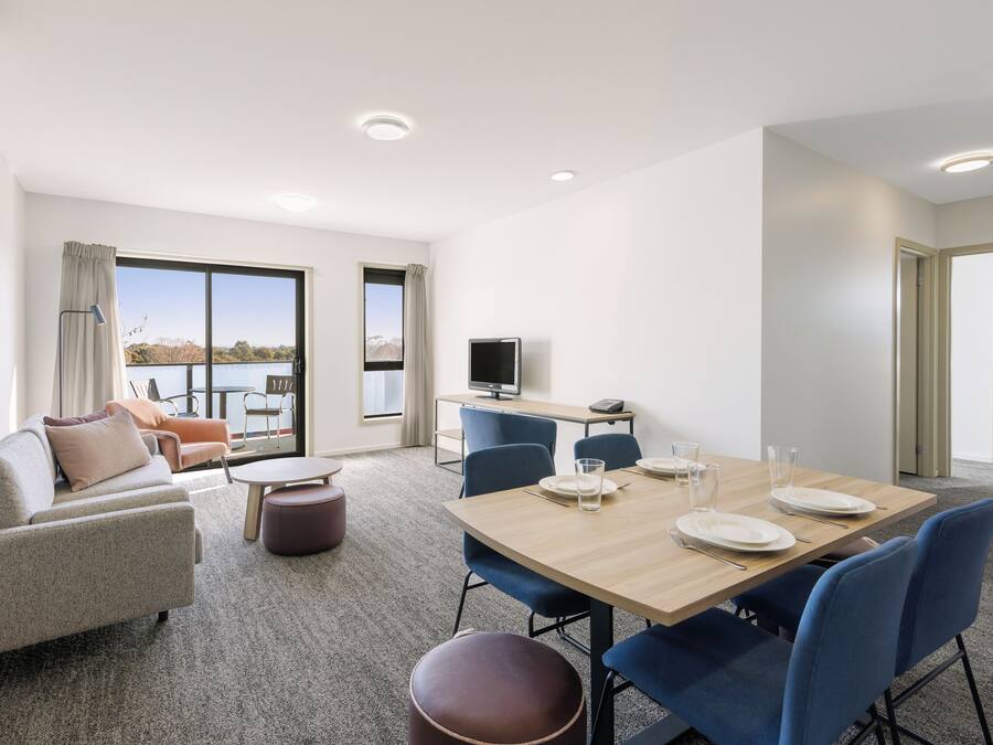 A modern hotel room with a dining area, a sofa, a TV, and a view of the outdoors.