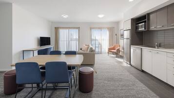Une chambre d’hôtel moderne dotée d’un coin repas, d’une kitchenette et d’un espace salon avec un canapé et des fauteuils.