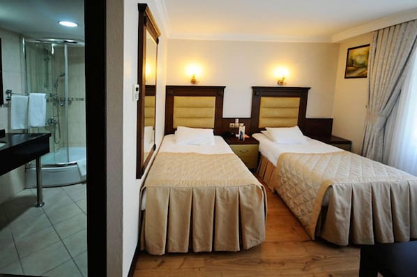 Habitación de hotel con dos camas, ducha, escritorio y espejo.