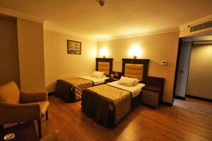 Una habitación de hotel con dos camas individuales, una silla, una mesita de noche y una puerta.