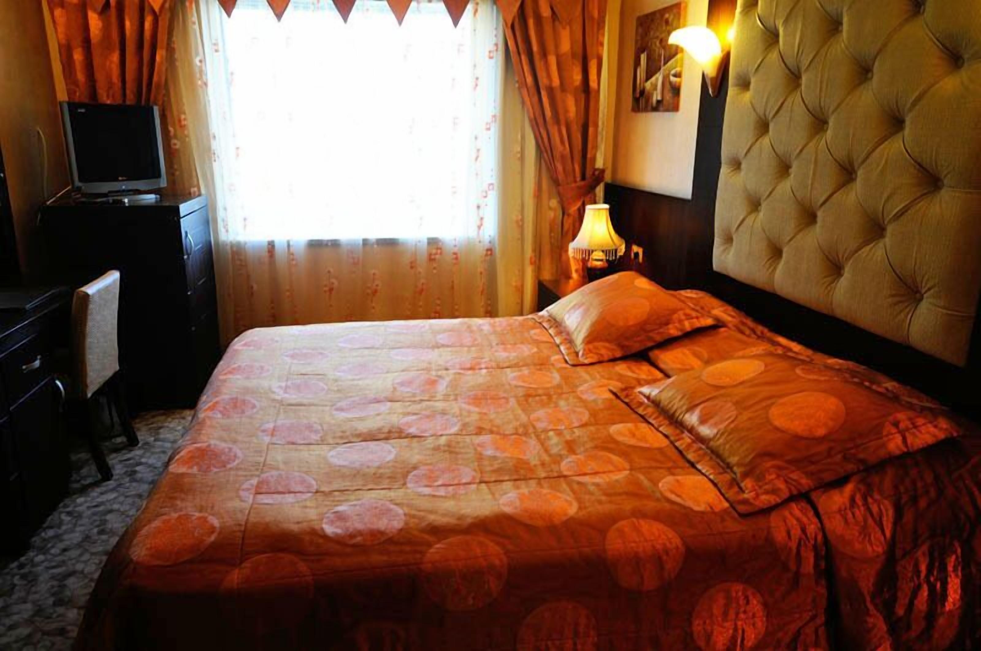 A hotel room with a bed, a television on a desk, and a lamp.