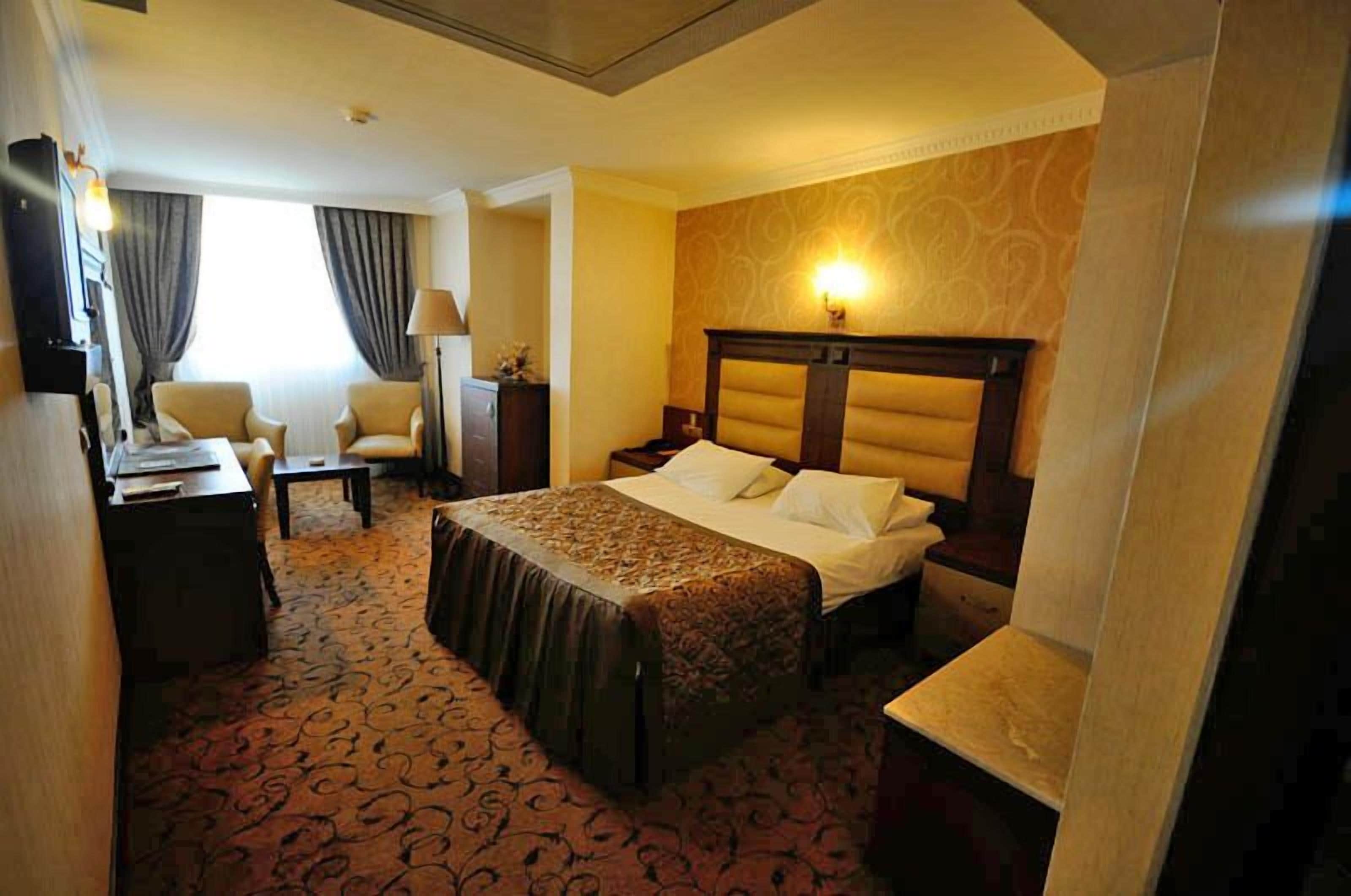 Une chambre d’hôtel avec un grand lit, un bureau, une chaise, une table de chevet et une lampe.