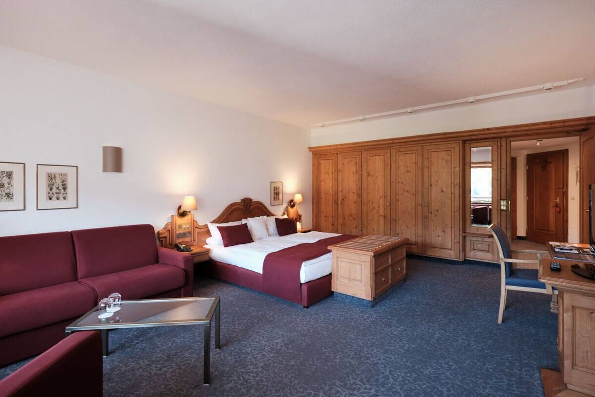 Ein Hotelzimmer mit einem Bett, einem roten Sofa, einem Holzkasten, einem Schreibtisch und einem Sessel.