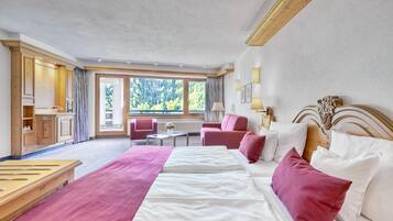 Ein Hotelzimmer mit einem großen Bett, zwei Sesseln, einem kleinen Tisch und Blick ins Freie.