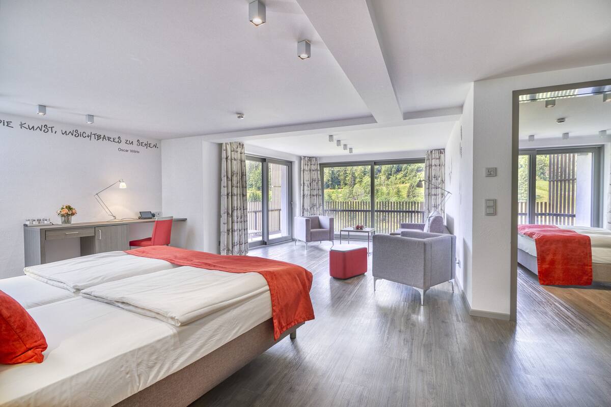 Ein modernes Hotelzimmer mit einem großen Bett, einem Schreibtisch, einem Stuhl und einem Balkon mit Blick auf Grünflächen.