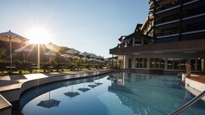 A swimming pool with sun reflecting on the water, surrounded by lounge chairs and umbrellas.