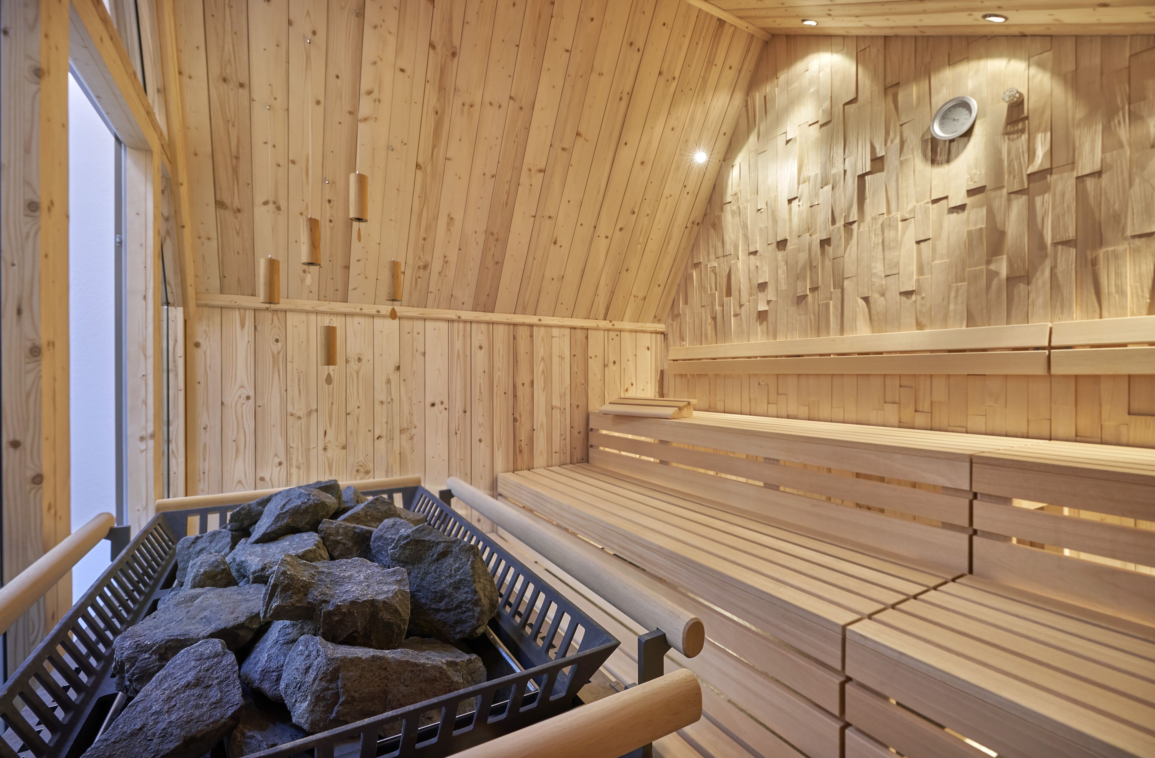 Ein Saunaraum mit Holzwänden und -bänken, eine Holzbank mit Steinen und einer an der Wand befestigten Uhr.