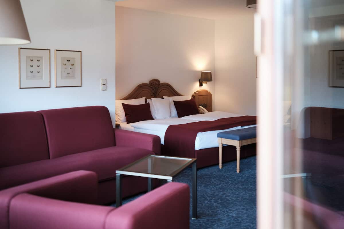 Ein Hotelzimmer mit einem großen Bett, zwei roten Sofas, einem kleinen Tisch und einer Lampe.