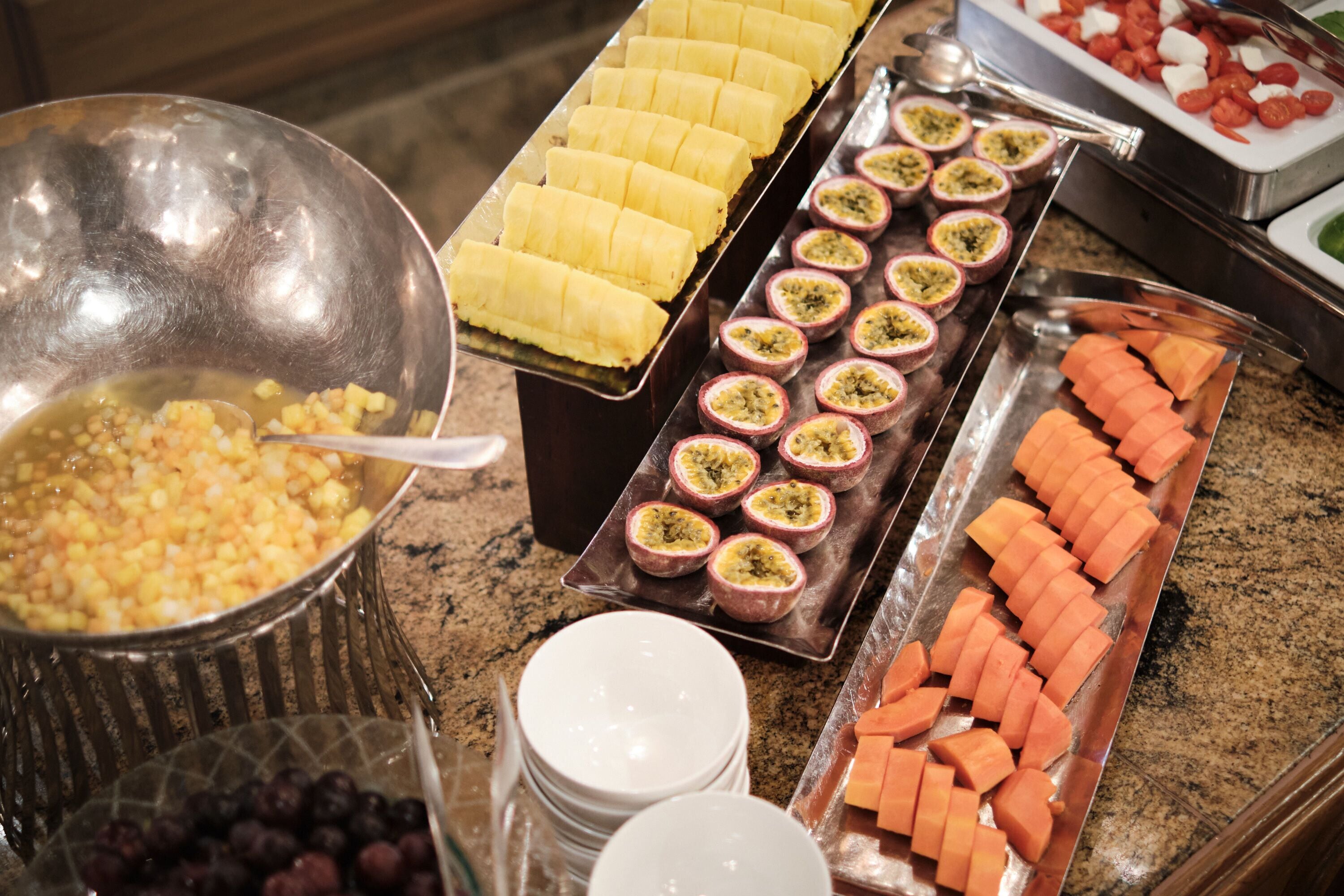 A buffet with various food items including sliced bananas, passion fruit, and carrots.