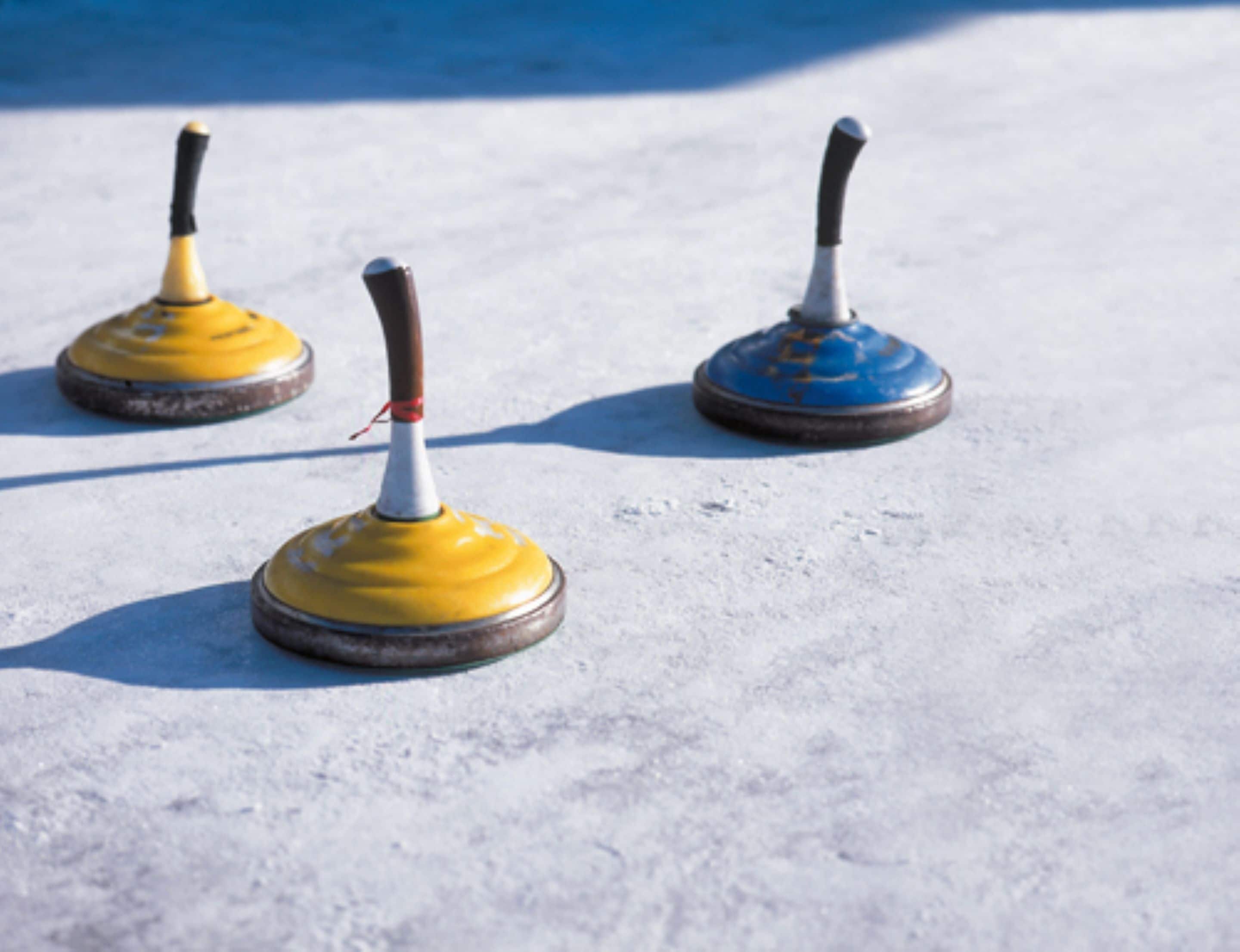 Três pedras de curling sobre uma superfície lisa e clara.