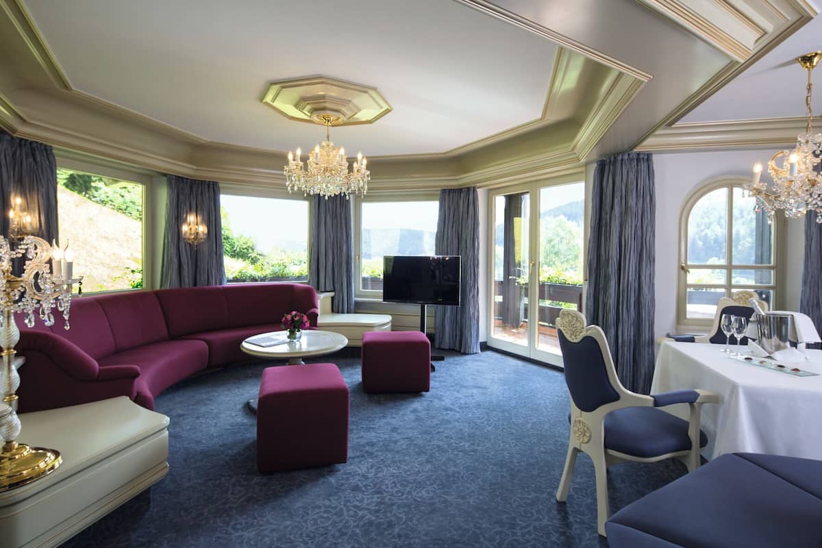 Ein luxuriöses Zimmer mit einem roten Sofa, einem Fernseher und einer Essecke mit Tisch für zwei Personen.