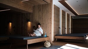 Un spa moderno con paredes de madera, una persona relajándose en un banco y una mesa de masaje al fondo.