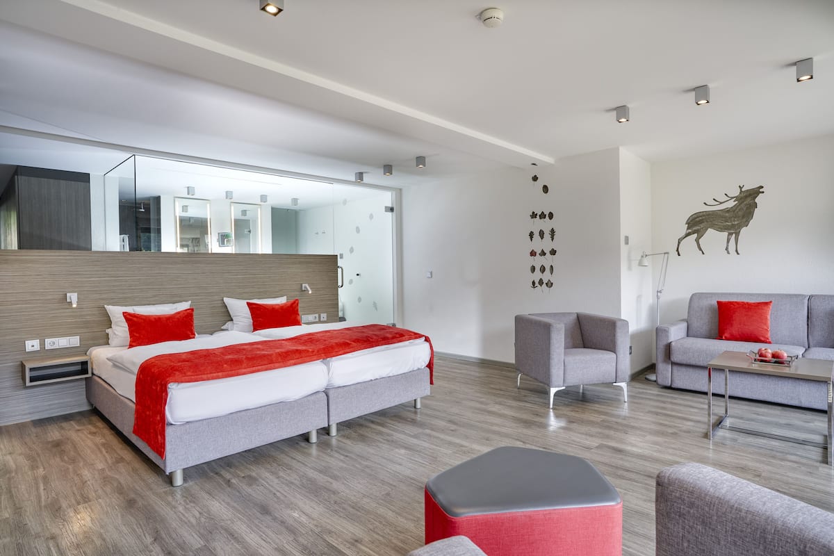 Ein modernes Hotelzimmer mit einem großen Bett, einer Couch, einem Sessel, einem kleinen Tisch und einem wandmontierten Spiegel.