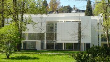 Ein modernes Gebäude mit großen Glasfenstern und einem Flachdach, umgeben von einer Grünfläche mit Bäumen.